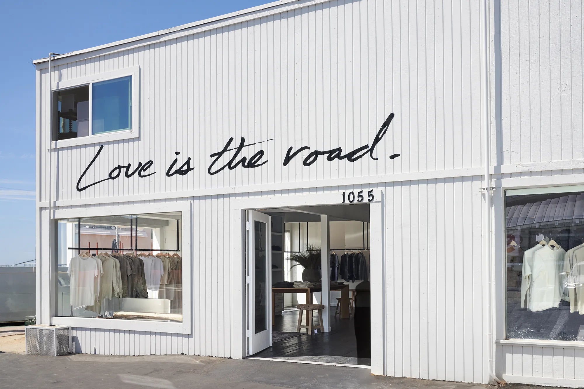 A white storefront building with large windows, a central open doorway, and black script text reading 'Love is the road.' across the facade.