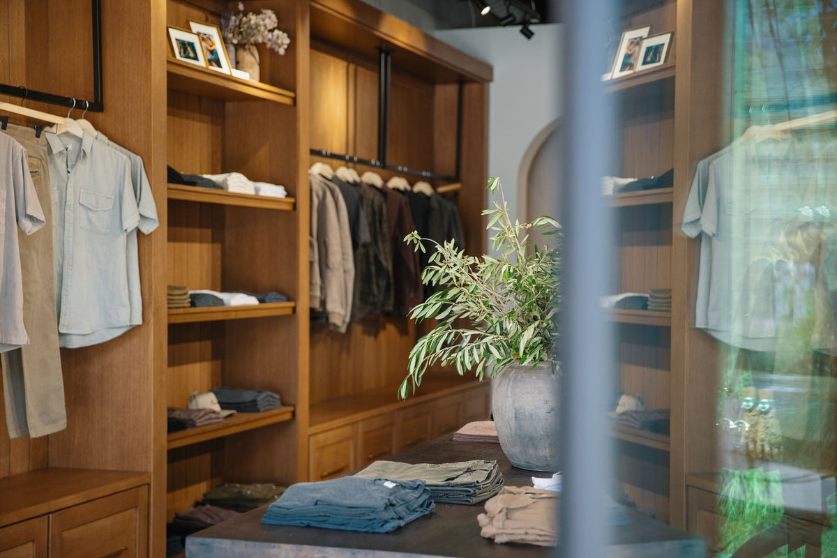 Clothing store interior with wooden shelves, hanging clothes, and a plant.